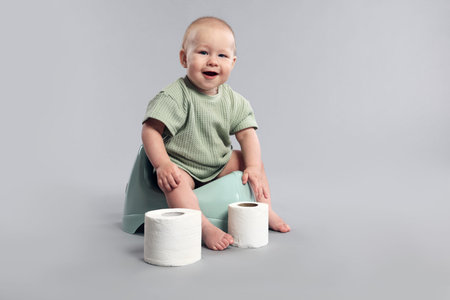 Cute little baby sitting on potty against light grey background