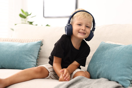Cute little boy in headphones on sofa at home