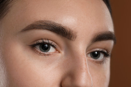 Young woman with beautiful eyebrows on brown background, closeup