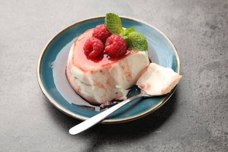 Delicious panna cotta with berries, sauce and mint on grey textured table, closeup