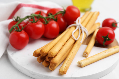Delicious grissini sticks and fresh tomatoes on white table, closeup