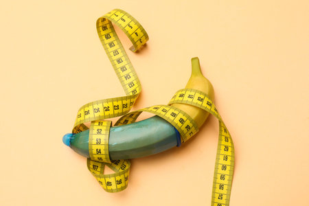 Banana with condom and measuring tape on beige background, top viewの写真素材