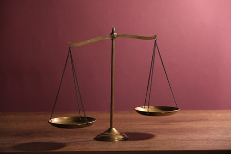 Scales of justice on wooden table against color background