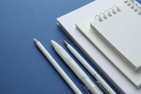 White notebooks, pencil and pens on blue background, closeup