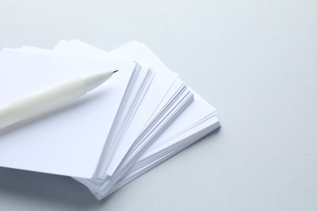 White pen and note papers on light grey background, closeup