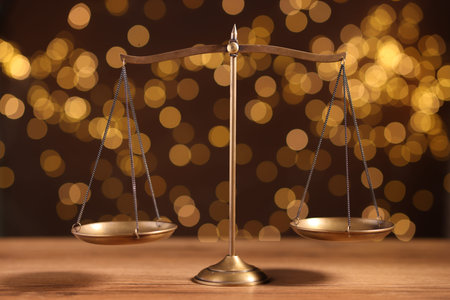 Golden scales of justice on wooden table against blurred lights