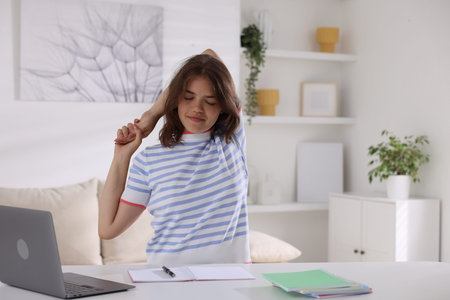 Beautiful teenage girl stretching at table indoors, space for text