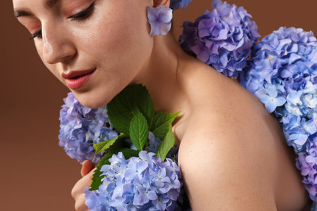Beautiful young woman with hortensia flowers on brown background, closeup