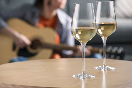 Glasses with white wine on table and man playing guitar indoors, selective focusの写真素材