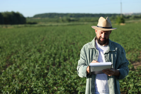 Farmer with clipboard in field of unripe soy outdoors, space for textの写真素材