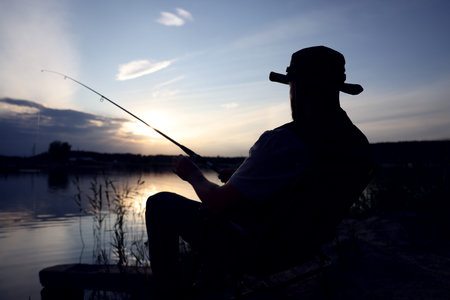 Fisherman with rod fishing near lake at sunsetの写真素材