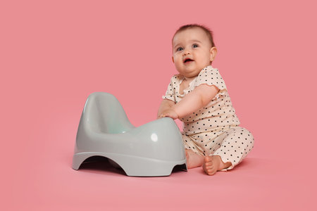 Cute little baby sitting near potty on pink backgroundの写真素材