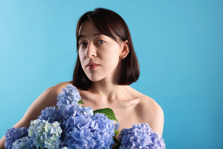 Beautiful young woman with hortensia flowers on light blue backgroundの写真素材