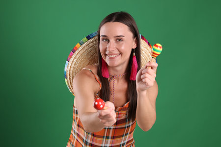 Smiling woman with sombrero hat playing maracas on green backgroundの写真素材