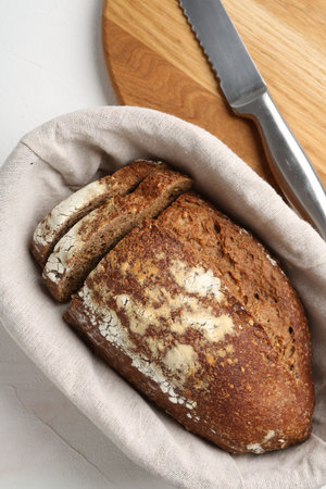 Fresh rye bread in basket on white textured table, flat lay