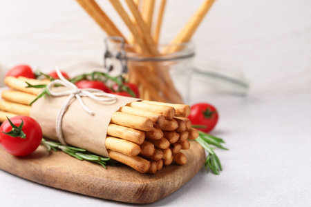 Delicious grissini sticks, rosemary and fresh tomatoes on light table, closeup