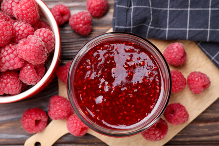 Sweet raspberry jam in glass jar and berries on table, flat lay