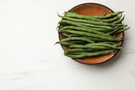 Fresh pea pods in bowl on white marble table, top view. Space for text