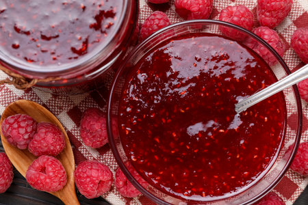 Sweet raspberry jam in glassware and berries on table, flat lay