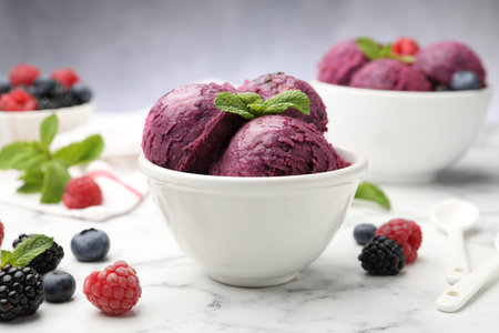 Delicious sorbet in bowl, fresh berries and mint on white marble table against grey background,...