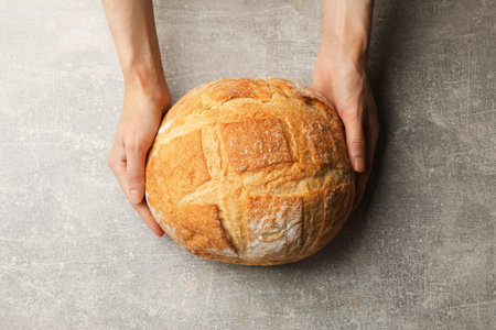 Woman with loaf of fresh bread at gray table, top view