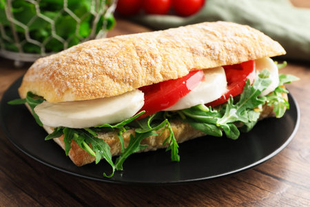 Delicious sandwich with mozzarella cheese, tomato and arugula on wooden table, closeupの写真素材