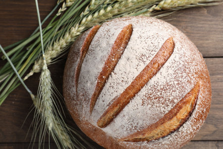 Fresh bread and green wheat spikes on wooden table, flat lay