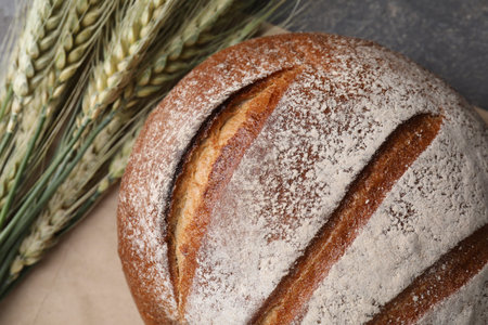 Fresh bread and green wheat spikes on gray table, flat lay