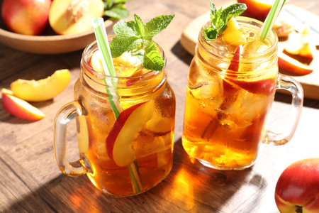 Refreshing iced peach tea with mint in mason jars and fresh fruits on wooden table, closeupの写真素材