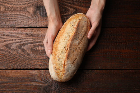 Woman with loaf of fresh bread at wooden table, top view