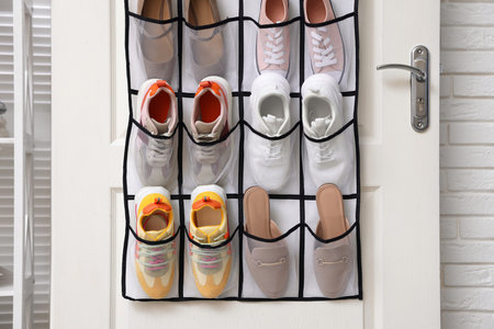 Organizer with different footwear on door indoors. Shoe storage
