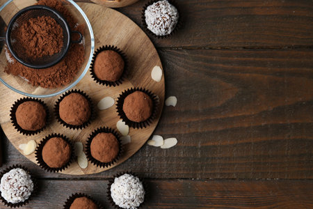 Delicious homemade candies with cocoa powder and coconut flakes on wooden table, flat lay. Space for...