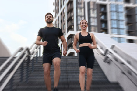 Woman and man in sportswear running down on stairs outdoors, motion blue effect. Low angle view