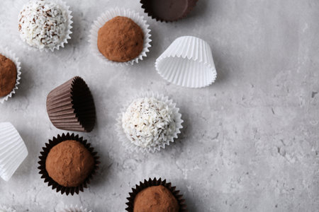 Delicious homemade candies with cocoa powder and coconut flakes on light gray table, flat lay. Space...
