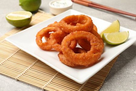 Fried squid rings, lime, sauce and chopsticks on gray table, closeupの写真素材