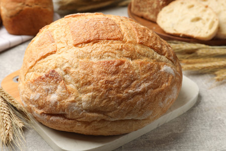 Fresh bread and wheat spikes on gray table, closeup