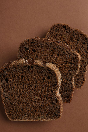 Pieces of fresh rye bread on brown background, top view