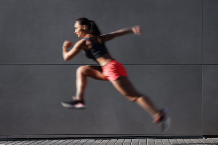 Woman in sportswear running near building outdoors, motion blur effect