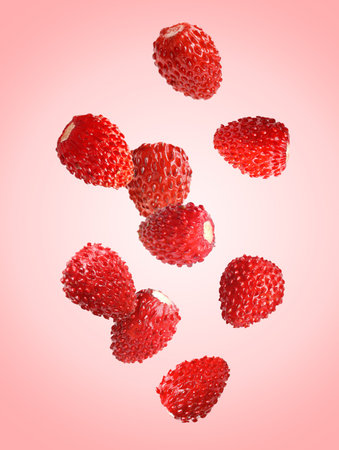 Fresh ripe wild strawberries falling against pink background