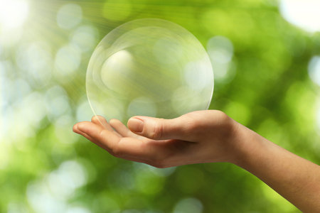 Hand holding a crystal ball against a blurred green background, closeup