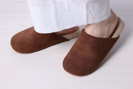 Woman in soft brown slippers on light wooden floor, closeup