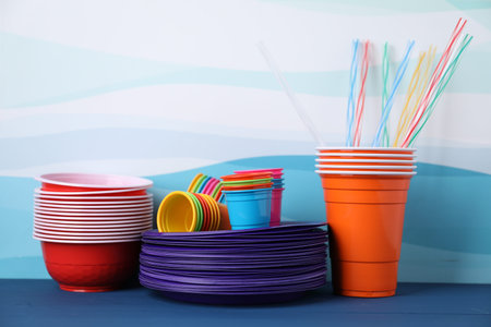 Set of disposable plastic dishware on blue wooden table against color background