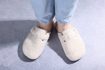 Woman in stylish white slippers on grey textured floor, closeup