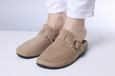 Woman in stylish beige slippers on light floor against grey background, closeup