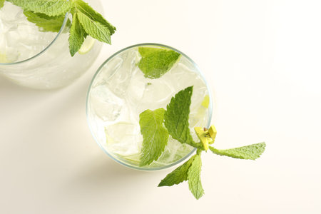 Tasty cocktail with lime and ice cubes on white table, flat lay