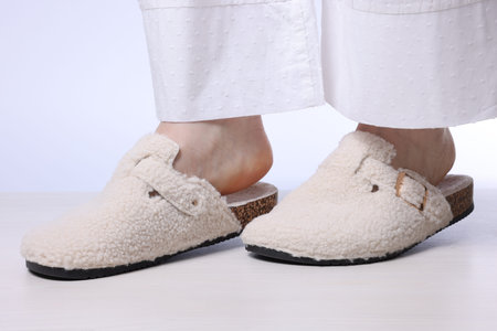 Woman in soft slippers on light wooden floor against white background, closeup