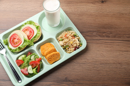 School lunch. Plastic tray with tasty food, milk and fork on wooden table, above view. Space for textの写真素材