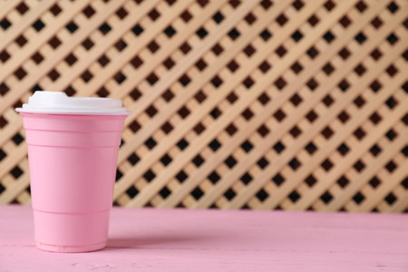 Disposable plastic cup on pink wooden table, space for text