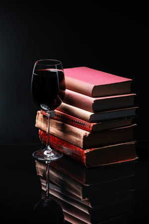 Red wine in glass and stack of books on mirror table against black backgroundの写真素材