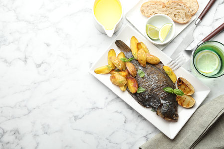 Homemade seafood dish. Tasty roasted flounder fish served with potatoes, basil and lemon slices on...